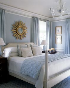 a bedroom with blue walls, white bedding and a sun mirror on the wall