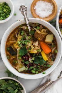 two bowls filled with soup and vegetables on top of a white countertop next to silver spoons