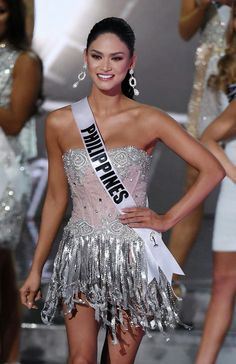 a woman in a silver and white dress on the runway with other models behind her