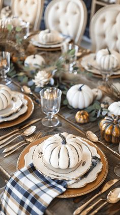 a table set with white pumpkins and plaid napkins, gold plates and silverware