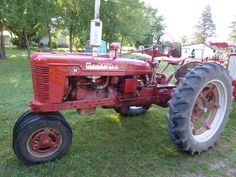 an old red tractor is parked in the grass