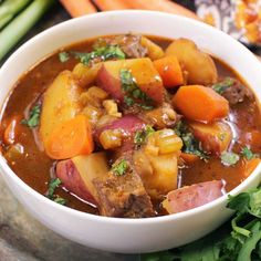 a bowl of stew with carrots, potatoes and celery on the side