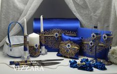 a table topped with blue and gold items next to a white rose, candle and napkins