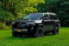 a black toyota 4runner is parked in the middle of some green grass and trees