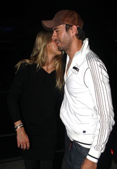 a man and woman standing next to each other in front of a car at night