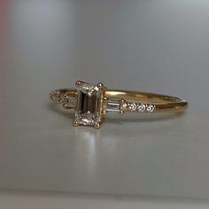 an engagement ring with two baguettes and three side stones on the band, sitting on a white surface