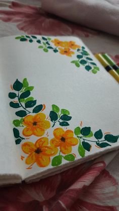 an open notebook with flowers painted on it and two pencils next to the book