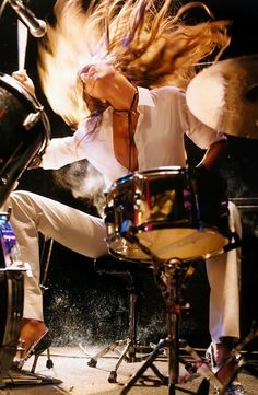 a woman with her hair blowing in the wind while sitting on a drum set and playing drums