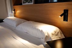 a bed with white sheets and pillows in a bedroom next to a wall mounted light