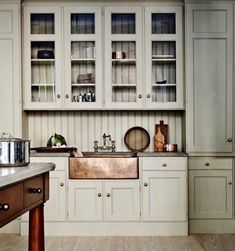 a kitchen with wooden floors and white cupboards on the wall, along with a copper sink