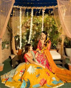 two women sitting next to each other in front of a bed with flowers on it