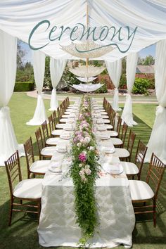 a long table set up with white linens and flowers on it for an outdoor wedding