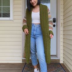 a woman standing in front of a door wearing a green cardigan sweater and jeans