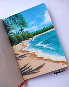 an open notebook with a painting of a beach and palm trees on the cover is shown