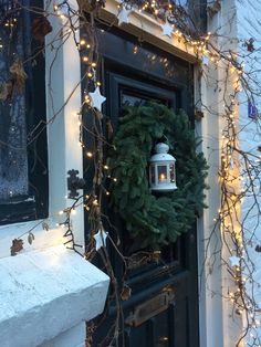 a wreath on the front door of a house decorated with christmas lights and garlands