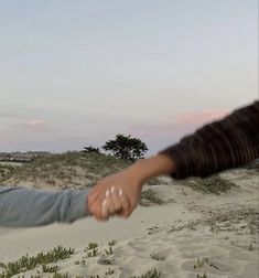 two people are holding hands in the sand