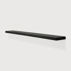 a long black shelf sitting on top of a white wall in front of a gray background