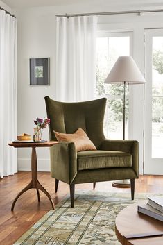 a living room with a chair, table and lamp on the hardwood floor in front of a window