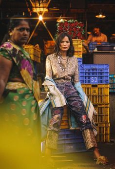 a woman sitting on top of a pile of crates in front of a man standing next to her