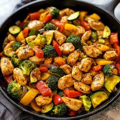 a skillet filled with chicken, broccoli, peppers and zucchini