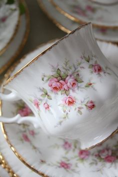 an antique tea cup and saucer with pink roses on it, surrounded by gold trimmings