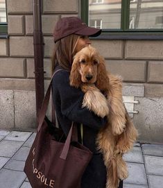 a woman holding a dog in her arms while standing on the sidewalk next to a pole