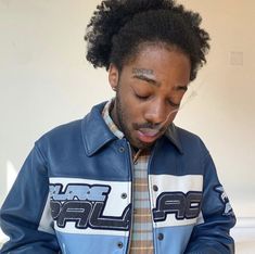 a man wearing a blue jacket looking at his cell phone while standing in front of a white wall