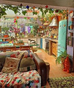 a living room filled with furniture and lots of plants hanging from the ceiling next to a refrigerator