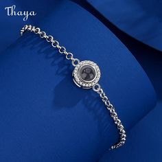 a silver bracelet with a black stone in the center on a blue background, that says thaya