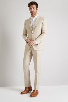 a man in a tan suit and brown shoes is standing with his hands in his pockets