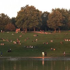 many people are sitting on the grass by the water and some have fallen asleep in the sun