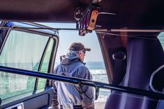 a man standing in the back of a truck looking out at the ocean from inside