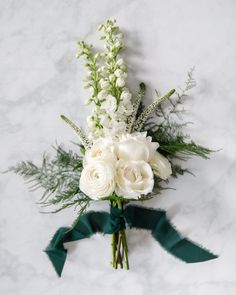 a bouquet of white flowers and greenery on a marble surface with a green ribbon