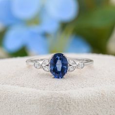 a blue and white diamond ring sitting on top of a piece of cloth with flowers in the background