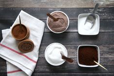 four bowls with different types of chocolate and cocoa powder in them on top of a wooden table