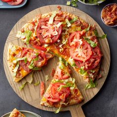 a pizza with tomatoes, lettuce and other toppings on a cutting board