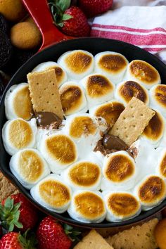 a bowl filled with marshmallows and crackers on top of strawberries