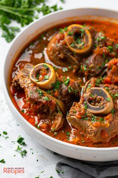 a white bowl filled with stew and meats on top of a black napkin next to some parsley