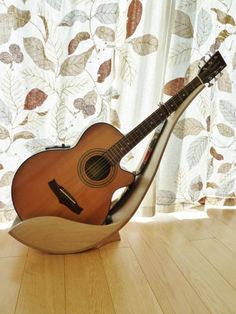 an acoustic guitar sitting on top of a wooden floor next to a window with curtains behind it