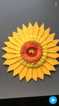 a yellow and red paper sunflower on a gray surface with an orange circle in the center