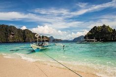 two boats in the water on a beach near some rocks and sand with blue sky