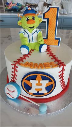 a baseball themed cake with the number one on it and a teddy bear sitting on top