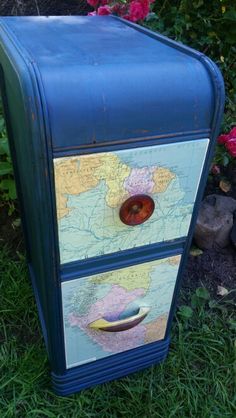 a blue painted dresser with a map on the top and bottom drawer, in front of some flowers