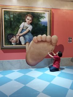 a woman kneeling down next to a giant foot in front of a painting on the wall