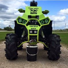 a green monster truck parked on top of a gravel road next to a grass covered field