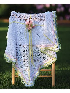 a crocheted blanket draped over a wooden chair in the grass with flowers on it