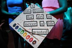 a graduation cap that has been decorated with words and paintbrushes in front of other people