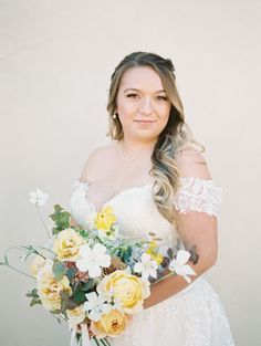 a woman in a wedding dress holding a bouquet of yellow and white flowers with long hair