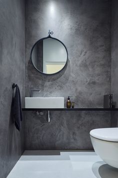 a white toilet sitting next to a bathroom sink under a round mirror on a wall