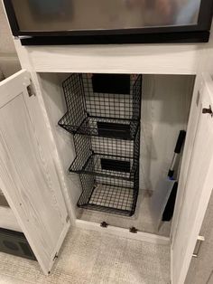 a tv mounted on top of a white wall next to a shelf filled with wire baskets